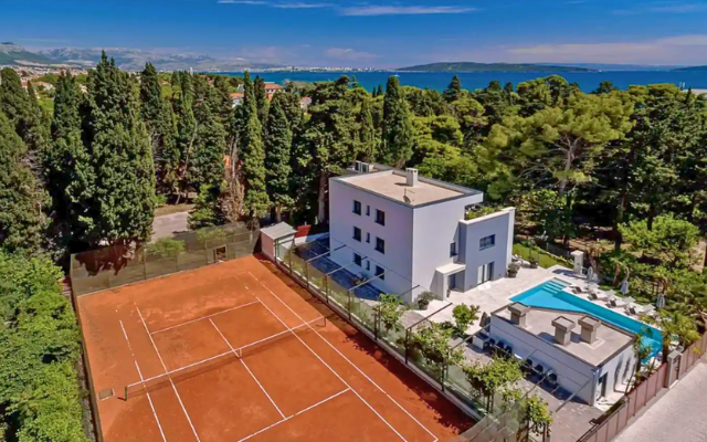 Villa surrounded by trees, the sea, and a clay tennis court