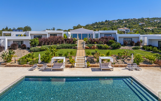 Modern-looking villa with steps leading down to a contemporary pool and gardens